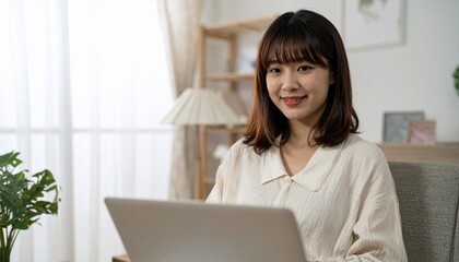 やさしい笑顔を見せる20代日本人女性がノートパソコンを操作する、静かな室内での落ち着きある上半身のポートレート

