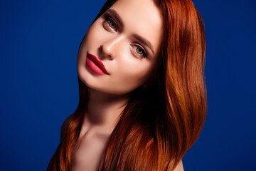 Fototapeta premium Portrait of a gentle young woman with red hair and glamorous makeup on a vibrant blue background