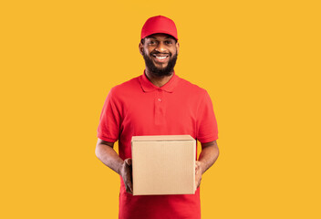 African American Delivery Man Holding Cardboard Box Delivering Online Order To Customer's Home Standing Over Yellow Background In Studio