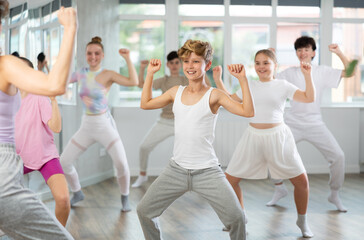 Fototapeta premium Teenage boy rehearse hip hop dance repeats movements of unrecognizable instructor performance with peers. Preparing for performance of choreographic team, practicing skills, repeating exercises