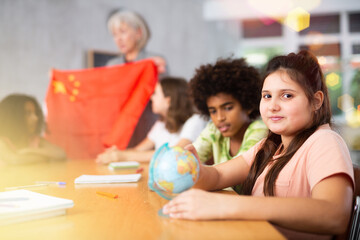 Fototapeta premium Ten-year-old schoolgirl is studying the history of China in lesson and an attentively is looking for her on the globe