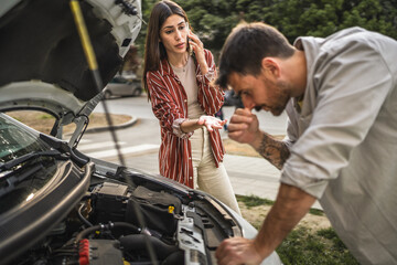 Boyfriend check car engine while girlfriend calls for assistance