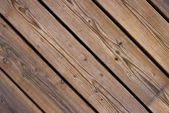 Top view of wooden floor texture. Diagonal wooden planks with grain, screw marks, nail heads typical for boardwalk or pier flooring
