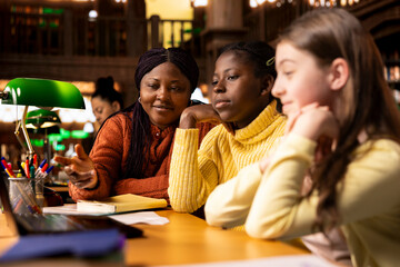 African american professor mentoring her teen girls students with an assessment, teaching academic concepts and enhancing their knowledge through practical exercises. Private lessons at the library.