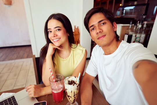 Happy latin couple taking a selfie while having refreshments in a cafe
