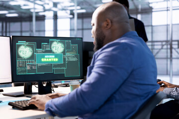 Access granted notification on monitor received by man reconfiguring server hub, optimizing it. African american data center IT expert using PC to successfully eliminate all errors