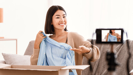 Content Creator. Smiling asian woman vlogger recording unpacking video on camera device at home,...