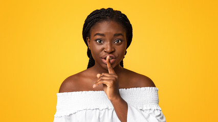 Keep silence. Young african american woman showing shhh sign at camera, holding finger near lips,...