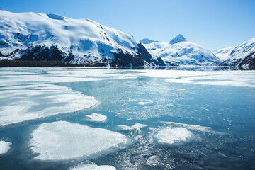 Ice covers a lake in Alaska, with mountains rising in the background.
