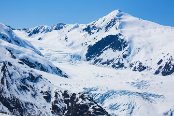 Snow-covered mountains bathe in sunlight, standing tall in the wilderness of Alaska.