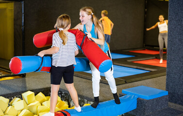 Children girls having fun and playing with inflatable sticks on the trampoline arena while spending...