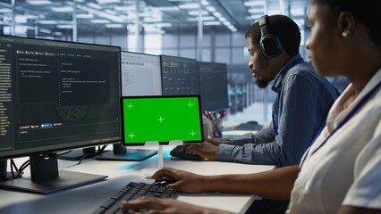 Fototapeta premium Team of programmer using green screen tablet, working in server farm to optimize it for data processing requirements. Teamworking colleagues coding on chroma key device in data center, camera A
