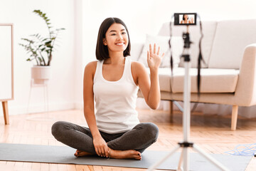 Fitness Blog. Portrait of sporty asian female trainer waving to camera, sitting on the floor on...