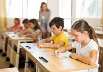 Portrait of cute intelligent schoolgirl who writing exercises at lesson in primary school