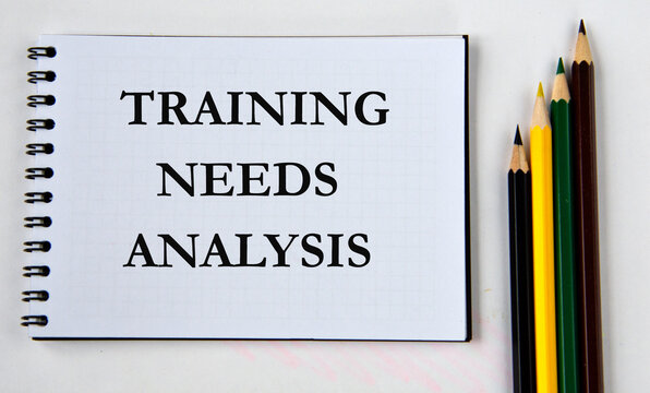 TRAINING NEEDS ANALYSIS - words in white notebook on white background with pencil
