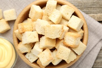 Tasty crispy croutons in bowl and sauce on wooden table, top view