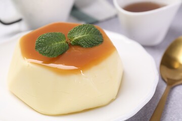 Delicious pudding with caramel sauce and mint served on light table, closeup