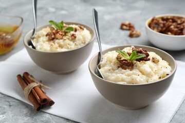 Delicious rice pudding with walnuts, cinnamon, mint and honey on grey table, closeup