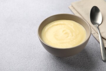 Tasty vanilla pudding in bowl and spoon on light grey table, closeup. Space for text