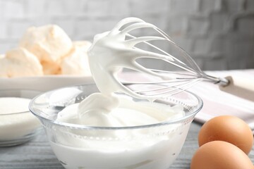 Whisk with whipped cream and other ingredients on gray table, closeup. Cooking meringue cookies