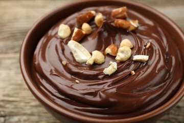 Delicious chocolate pudding with nuts in bowl on wooden table, closeup