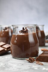 Tasty pudding in glass jars and pieces of chocolate on light grey table, closeup
