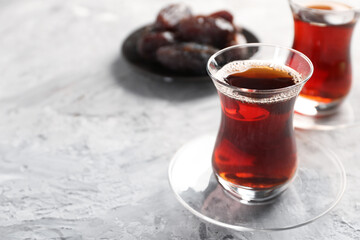 Traditional Turkish tea in glass cups and dates on light grey table, closeup. Space for text