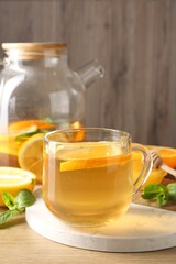 Aromatic fruit tea in glass cup, teapot, orange, lemon, honey and mint on wooden table, closeup