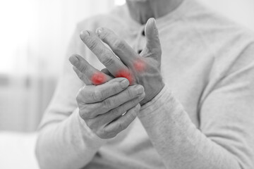 Arthritis. Man suffering from pain in fingers indoors, closeup. Black and white toning with red...