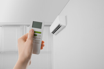 Fototapeta premium Woman using remote to control air conditioner in room, closeup