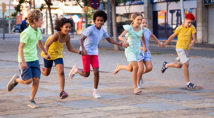 Group of smiling kids holding each other hands while running through city streets together.