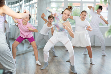 Female girl student repeats movements of unrecognizable teacher during group modern dance class. Hobbies, active pastime, additional extracurricular activities for children and teenagers