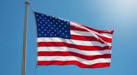 Obraz premium American flag waving against a clear blue sky on a sunny day with a metal flagpole visible