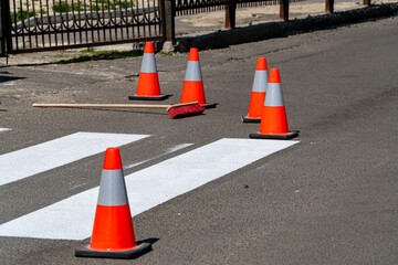 Brightly colored safety cones and a broom lie near freshly painted street lines under clear skies,...