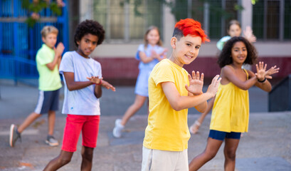 Obraz premium Cheerful young boy with dyed hair performing contemporary dance with his friends during rehearsal outdoors.