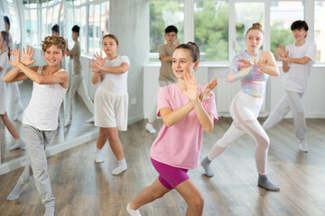 Female teen performs choreographic exercises and teaches energetic mobile social house dance together with friends. Young girls and guys in repeat movements, train in spacious studio