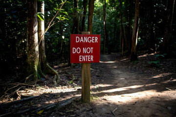 A red warning sign reading "Danger Do Not Enter" stands at the entrance to a forested path, cautioning visitors to stay away.