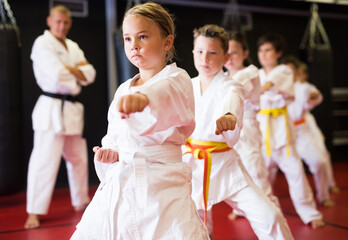 Kids in kimonos practicing effective karate techniques in group workout at training room