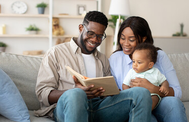 Fototapeta premium Leisure With Child. Caring Young Parents Reading Book To Their Adorable Infant Son Relaxing Together Sitting On Couch In Living Room, Happy Dad And Mum Bonding With Toddler Baby Kid At Home