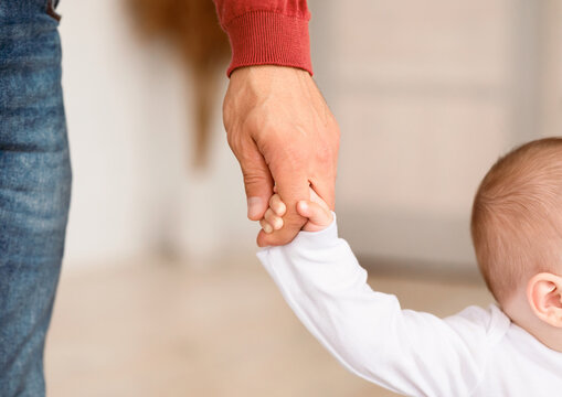 Father Holding Hand Of Little Baby Toddler Helping Child Make First Steps Standing At Home. Daddy's Support. Cute Family And Fatherhood Moments Concept. Cropped, Closeup - Powered by Adobe