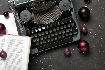 Vintage typewriter with Christmas balls and book on black background