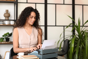 Young African-American author using typewriter at table in cafe