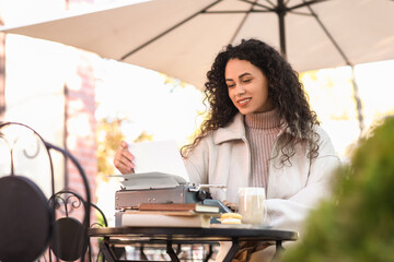 Young African-American author using typewriter at table in street cafe