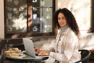 Young African-American author using laptop at table in street cafe