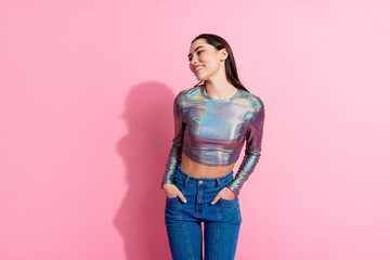 Young woman in a glossy cropped top and jeans posing against a bright pink background, expressing confidence