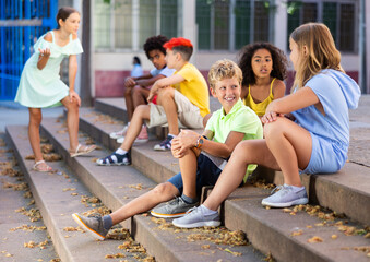Children talking together while sitting on stairs outdoors. Youngsters chatting during summer day.