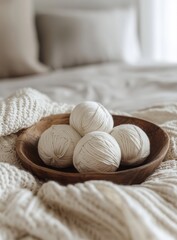 Soft, creamy white yarn balls rest in a wooden bowl, nestled on a cozy knitted blanket, on a bed