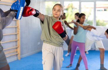 Focused girl hitting the focus mitts held by his boxing trainer