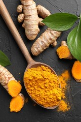 Aromatic turmeric powder in spoon, fresh roots and leaves on black table, flat lay