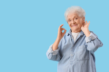 Senior woman with hearing aid showing OK on blue background